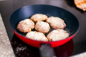 Homemade cutlets in frying pan cooking on induction hob.