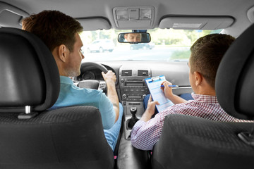 education, examination and people concept - driving school instructor with clipboard and male driver in car
