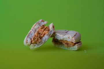 One broken macaron tastefully salted caramel on one-ton green background. French dessert. Sweets.