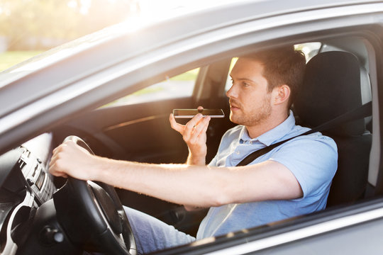 Transport, Vehicle And People Concept - Smiling Man Or Driver Driving Car And Recording Message Using Voice Command Recorder On Smartphone