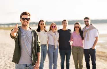 Fototapeta premium friendship, leisure and people concept - happy man with group of friends on beach in summer showing thumbs up