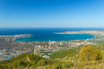 Fototapeta na wymiar Scenic view of Gelendzhik city and sea bay. Sunny day. Trees on hills on foreground. Photo of popular resort from hill of caucasian mountains.