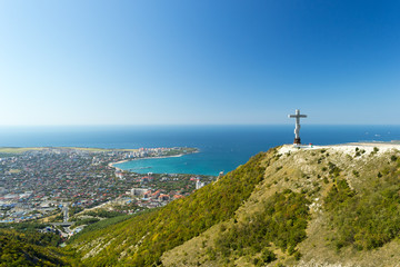 Scenic view of Gelendzhik resort city from hill of caucasian mountains. Worship cross monument with orthodox chapel in foundation on hill.
