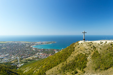 Fototapeta na wymiar Scenic view of Gelendzhik resort city from hill of caucasian mountains. Worship cross monument with orthodox chapel in foundation on hill.