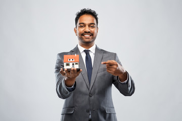 real estate business and people concept - indian man realtor with house model over grey background