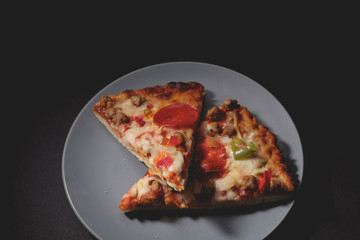 Two slices of hot pizza on blue-gray saucer with dark background
