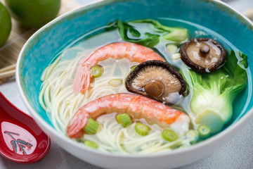 Turquoise bowl of panasian soup with shrimps, noodles, bok choy and shiitake mushrooms, close-up