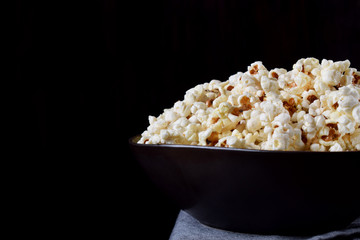 Popcorn in a black ceramic bowl on a wooden table against dark background