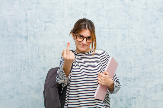 young student woman feeling provocative, aggressive and obscene, flipping the middle finger, with a rebellious attitude against grunge wall background