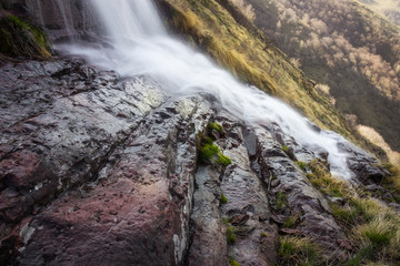 Low perspective, long exposure, close up composition of scenic Monk's jump waterfall on Old mountain, cascading down the sunlit dark red rocks