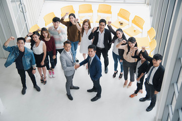 Young Asian business man smiling and felling happy are shaking hands which standing in front of people who standing  at the meeting room. Seminar and training concept. see from top view.