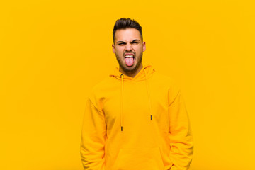 young hispanic man feeling disgusted and irritated, sticking tongue out, disliking something nasty...