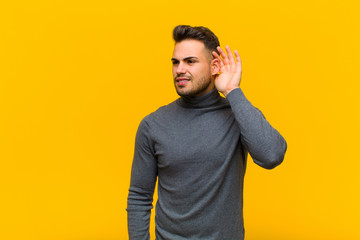 young hispanic man looking serious and curious, listening, trying to hear a secret conversation or...