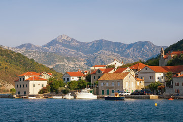 Beautiful autumn Mediterranean landscape. Small seaside village with red roofs at the foot of the mountains. Montenegro, Adriatic Sea, Bay of Kotor, Lepetane village
