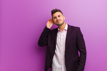 young hispanic man looking serious and curious, listening, trying to hear a secret conversation or...