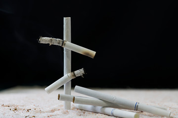 Cigarette butts white stacked in the form of a tombstone cross. There are several whole cigarettes...
