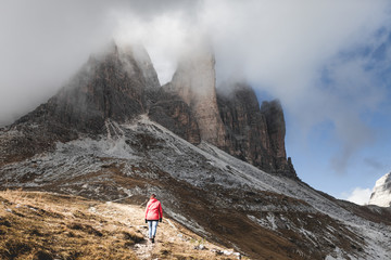 Female hiker with red jacket on a hike ontop a peak of tres cimes mountain in south tyrol. Motivational and inspirational scene. Cloudy and very contrasty dramatic edit.