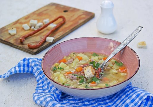 Yellow pea soup with potatoes, carrots, ham and smoked sausages in a clay bowl on a light concrete background. Served with white bread croutons.
