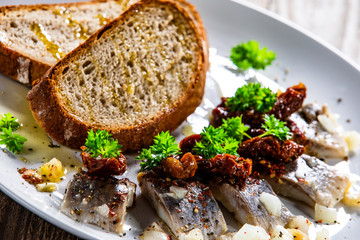 Marinated herring fillets with slices of bread on white plate on wooden table
