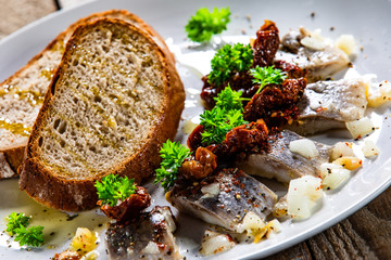Marinated herring fillets with slices of bread on white plate on wooden table