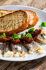 Marinated herring fillets with slices of bread on white plate on wooden table