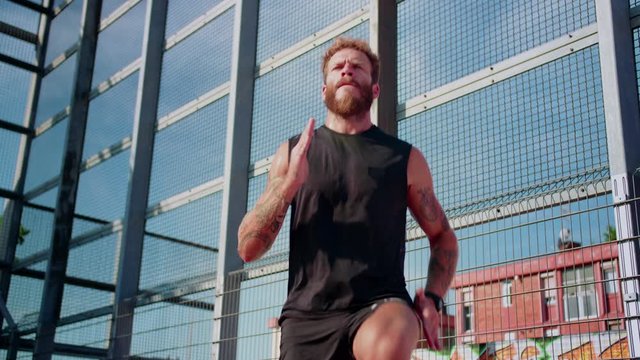 Motivated mixed race guy training doing activities outdoor at urban city landscape alone, dressed in total black sportswear looking straight with serious bearded face of active tattooed young man