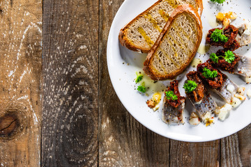 Marinated herring fillets with slices of bread on white plate on wooden table