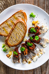 Marinated herring fillets with slices of bread on white plate on wooden table