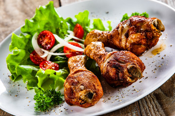 Grilled chicken drumsticks and vegetables on white plate