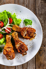 Grilled chicken drumsticks and vegetables on white plate