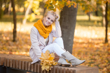 Portrait of pretty blonde teen girl with bouquet of yellow leaves sitting in autumn park