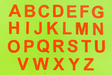 The letters of the English alphabet are cut from red cardboard on a green background