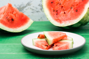Ready-to-eat sliced watermelon on a plate and uncut watermelon on a green wooden table