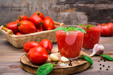 Ready-to-eat fresh tomato juice with basil leaves in glasses and tomatoes on a wooden table