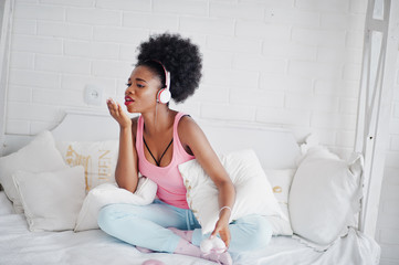 Fototapeta na wymiar Young african american woman sitting in bed and listen music on earphones.