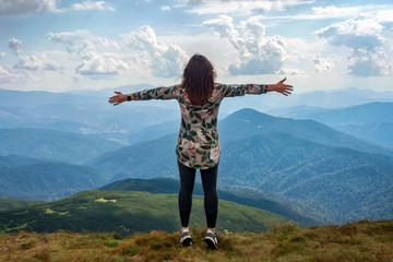 Girl traveling in mountains alone, standing with hands up achieving the top, welcomes a sun....