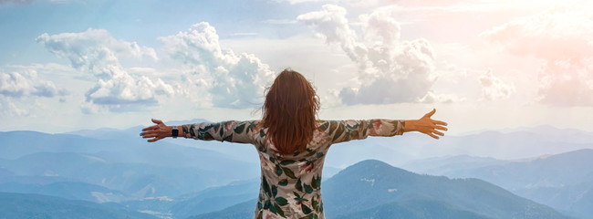 Girl traveling in mountains alone, standing with hands up achieving the top, welcomes a sun....