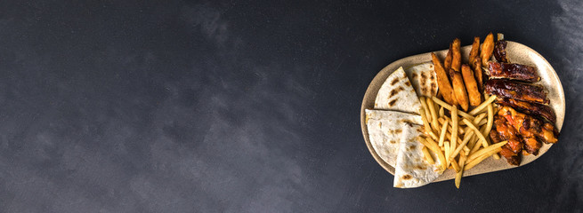 Fried pork ribs, french fries and pita bread on plate. Rustic food concept on grey texture background. Top view and Flat lay banner with copy space for text.