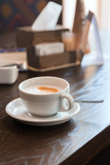 White cup of cappuccino on wooden table in restaurant stylish toning