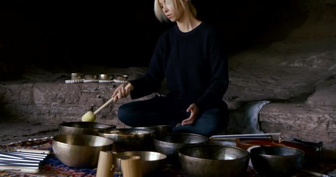 serious lady hits metal bowls with brown wooden hammer