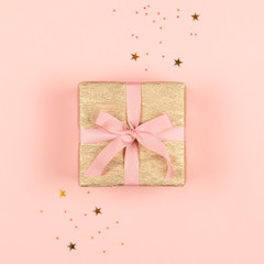 Golden gift box with pink bow on the pink background with sparkles.