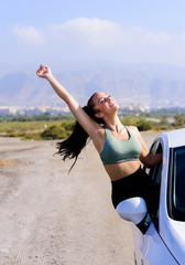 Portrait of happy young woman going on a road trip leaning out of window with Hair In Wind.