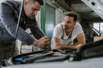 Fototapeta na wymiar Auto mechanics talking while analyzing a car engine in a workshop