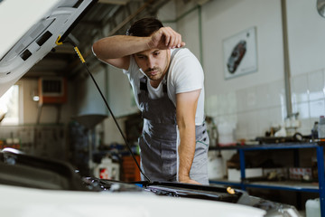 Tired auto mechanic analyzing car problems in a repar shop