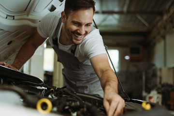 Young smiling auto mechanic examining engine in a workshop
