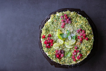 Top view on green cake with spinach and red cranberries on a plastic food tray. black background with copy space