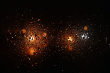 Fototapeta na wymiar Raindrops on foggy window. Night unfocused lights behind wet window