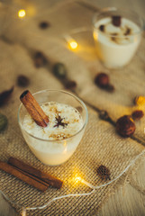 Eggnog in glasses with star anise and cinnamon on wooden table for Christmas and winter holidays. Copyspace included.