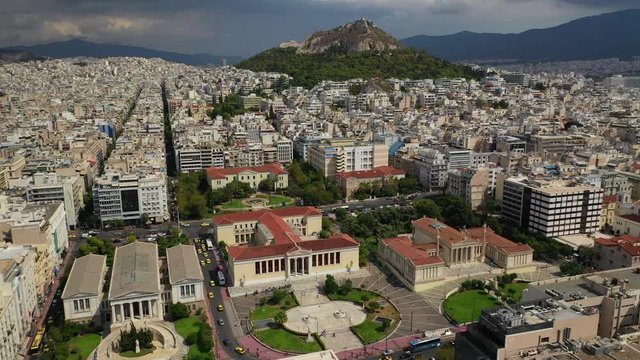 Aerial video of famous trilogy landmark buildings of Academy of Athens, Panepistimio or University, public Library with iconic Lycabettus hill at the background, Athens, Attica, Greece