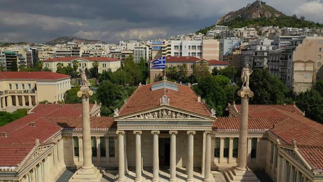 Aerial video of famous trilogy landmark buildings of Academy of Athens, Panepistimio or University, public Library with iconic Lycabettus hill at the background, Athens, Attica, Greece